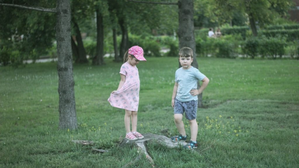 girl and boy standing beside trees during daytime